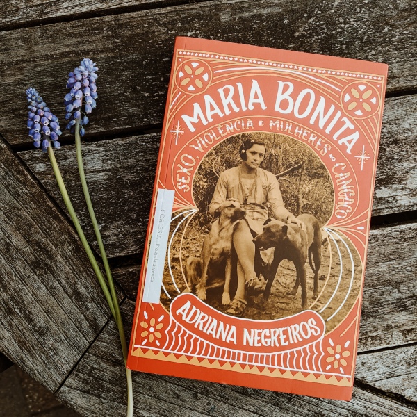 Livro Maria Bonita: sexo, violência e muheres no cangaço sobre uma mesa de madeira rústica, com dois ramos de lavanda ao lado à esquerda.